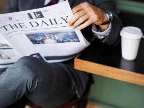 Businessman reading a "Daily" newspaper with coffee cup on table