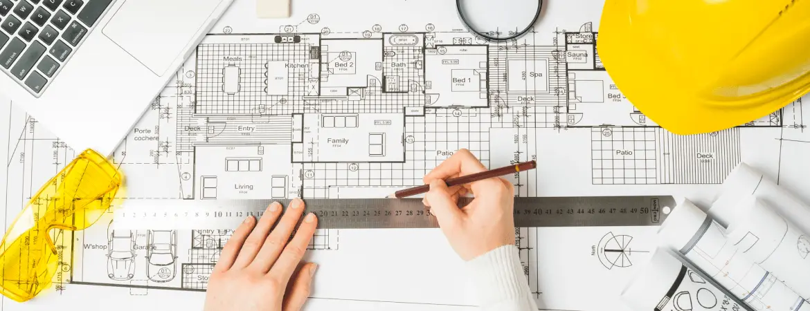 Construction blueprint with ruler and pencil on a desk, surrounded by safety helmet, rolled plans, and engineering tools.