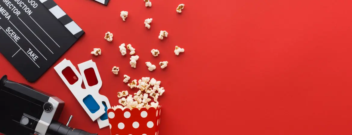 Movie entertainment concept with popcorn, film clapperboard, 3D glasses, and camera on red background.